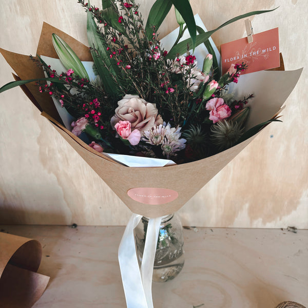 Bouquet of flowers wrapped in brown paper with a white ribbon on a wooden surface.
